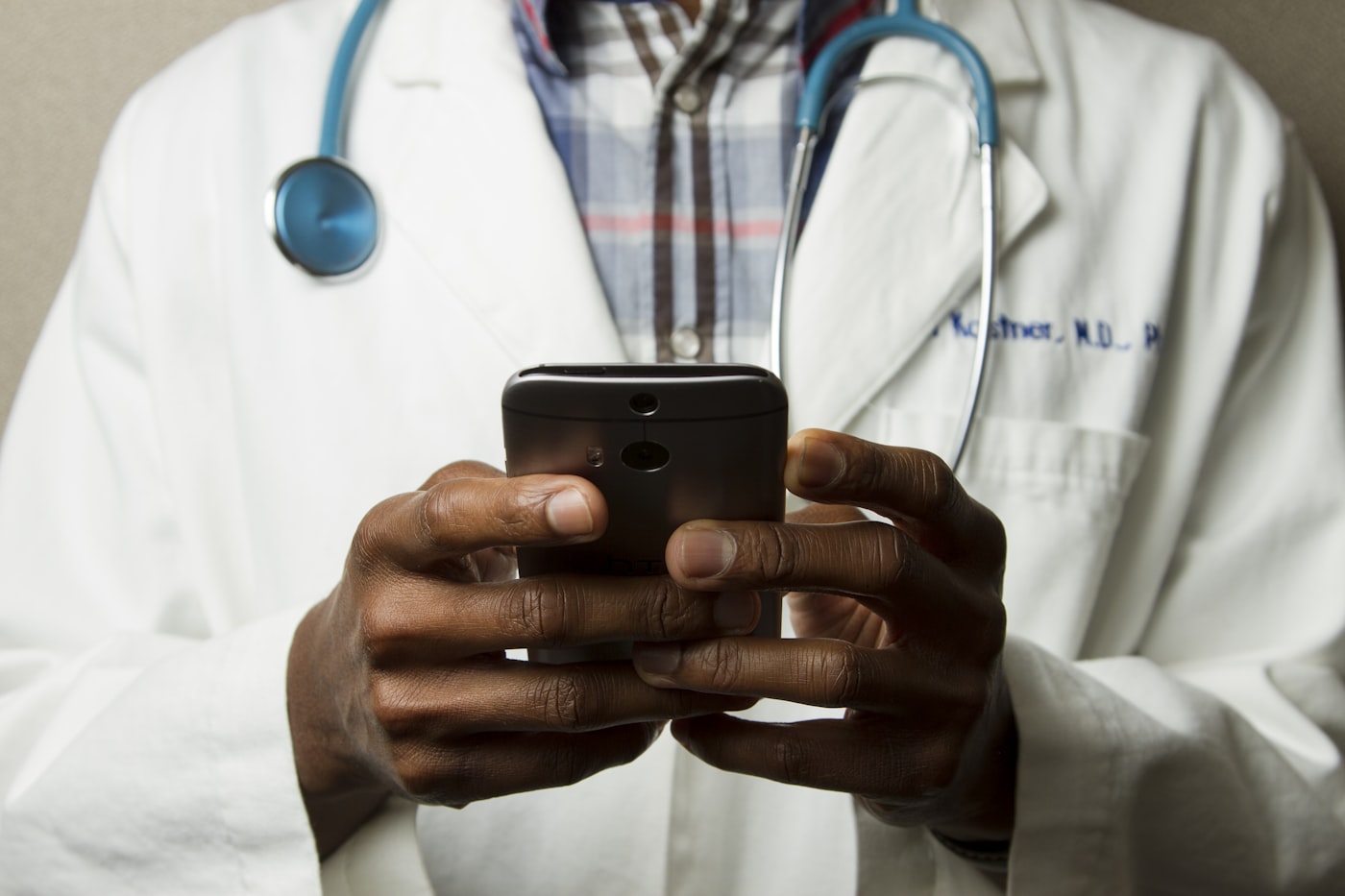 Clinician in a white coat with a stethoscope using a mobile device